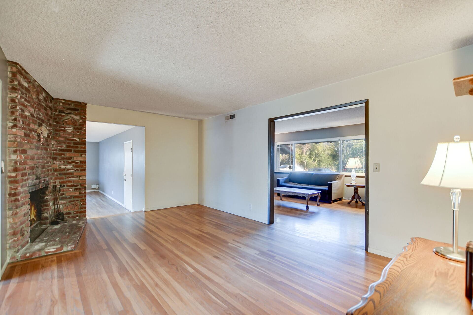Near-empty Claremont living room with a lit brick fireplace during a transition
