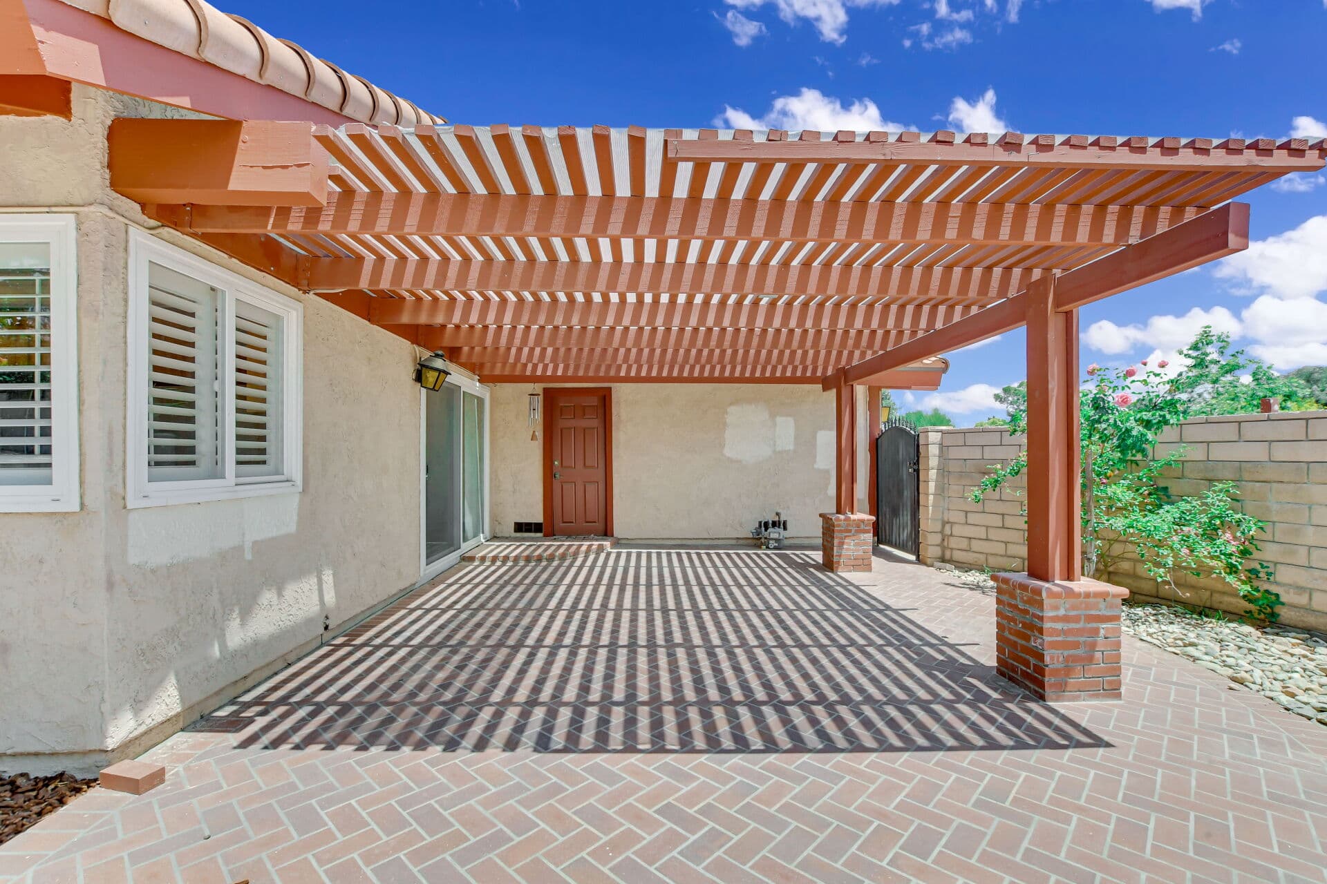 Terracotta pergola over a brick patio behind a Claremont home