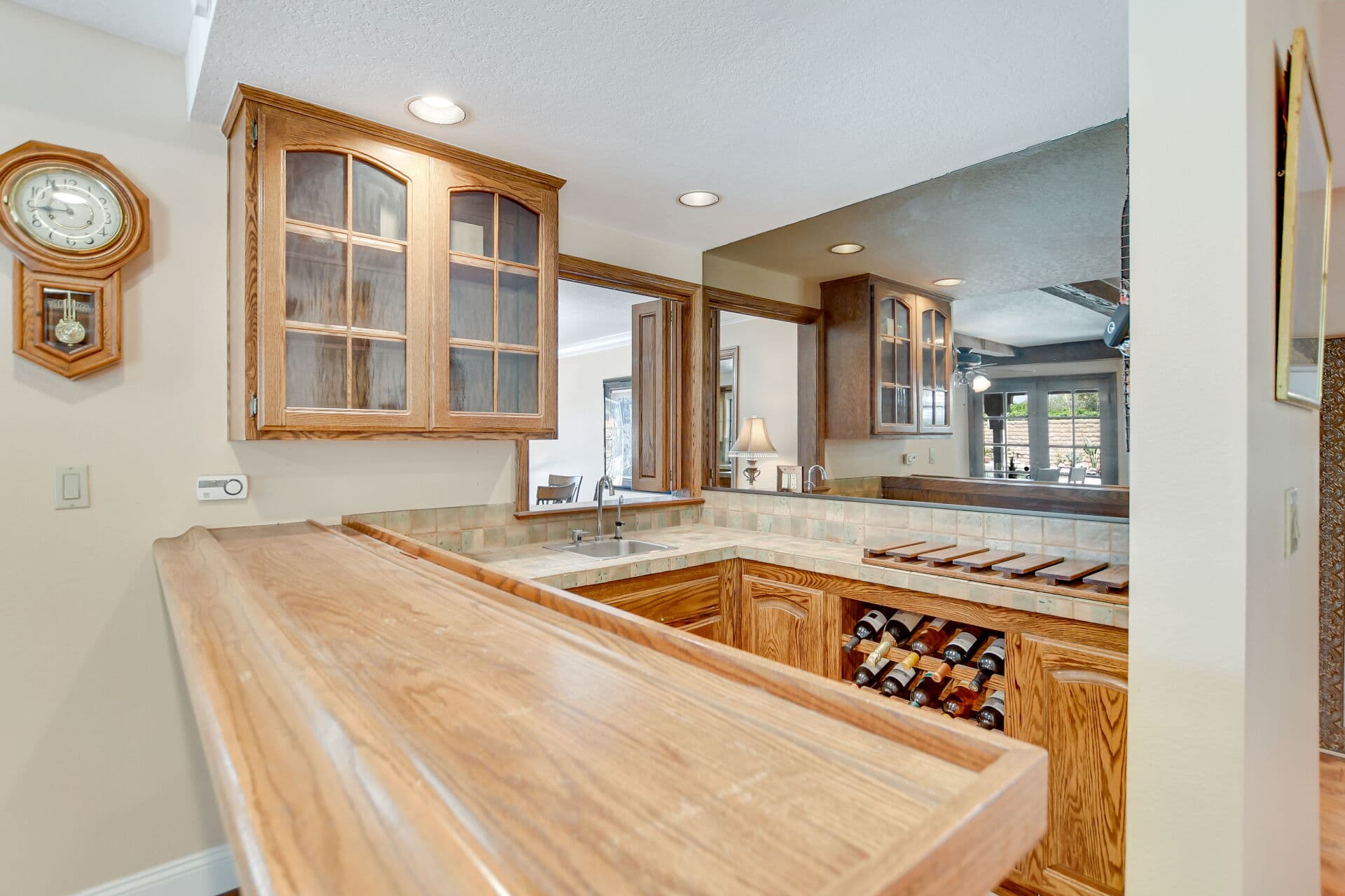Oak wet bar with glass-front cabinets and a wall clock in a Claremont home