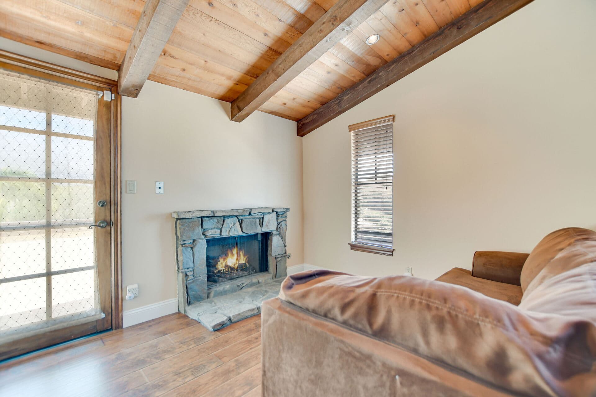 Den with a stone corner fireplace and glass door in a Claremont home