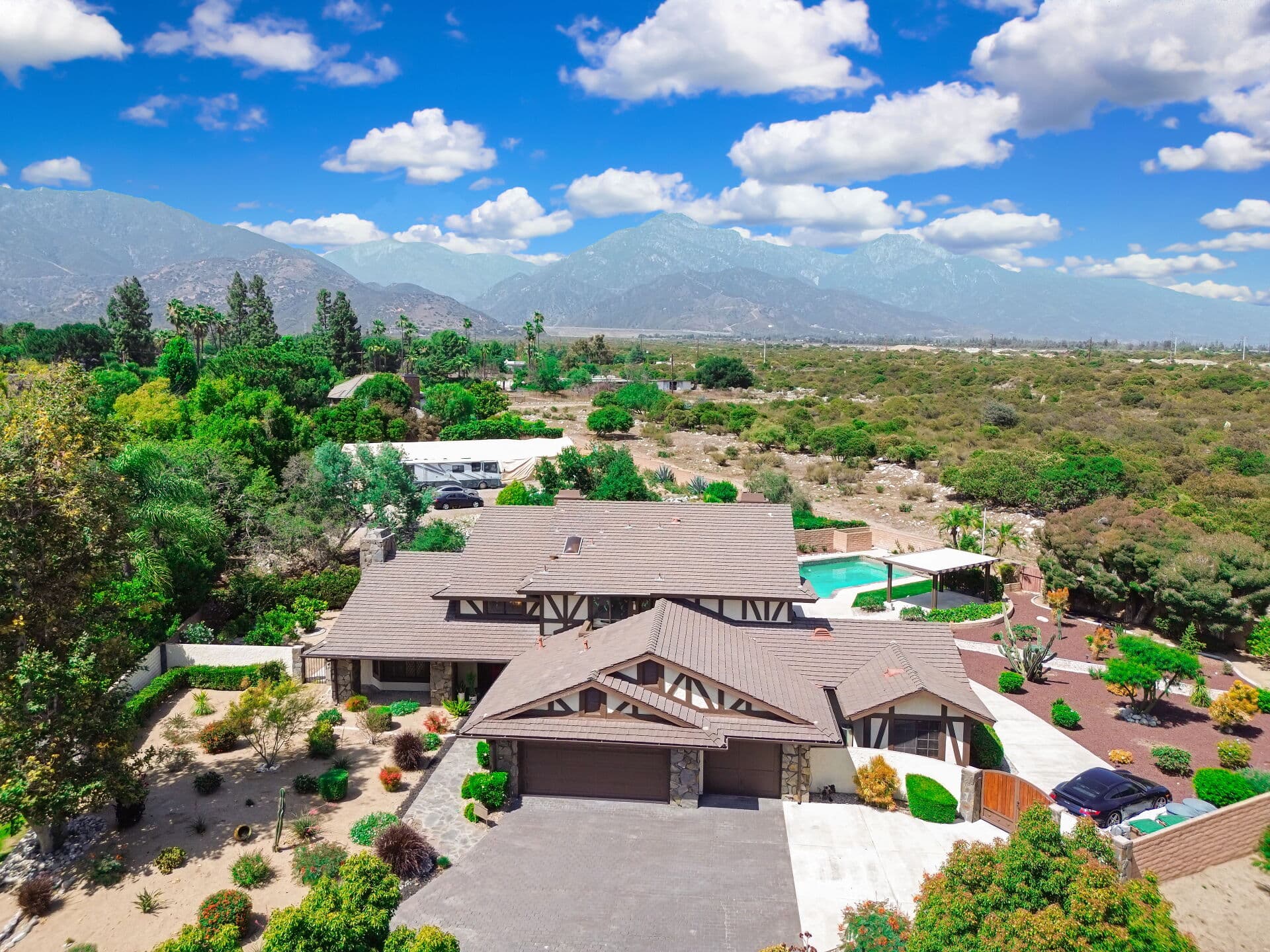Aerial view of a Tudor-style Claremont estate with pool, set against the San Gabriel Mountains