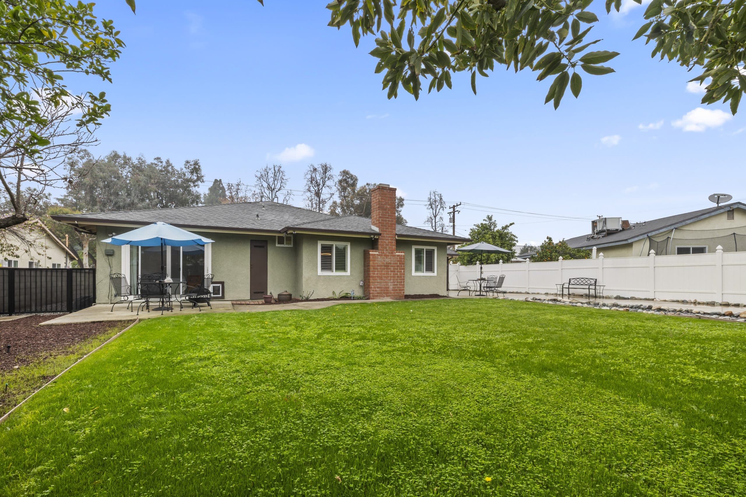 Fenced backyard and rear exterior of a Claremont ranch home with a brick chimney