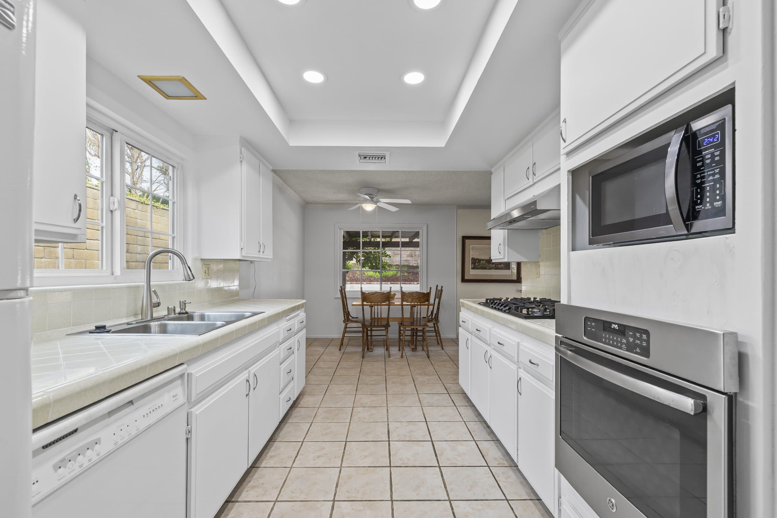Bright white galley kitchen opening to a sunny nook in a Claremont home