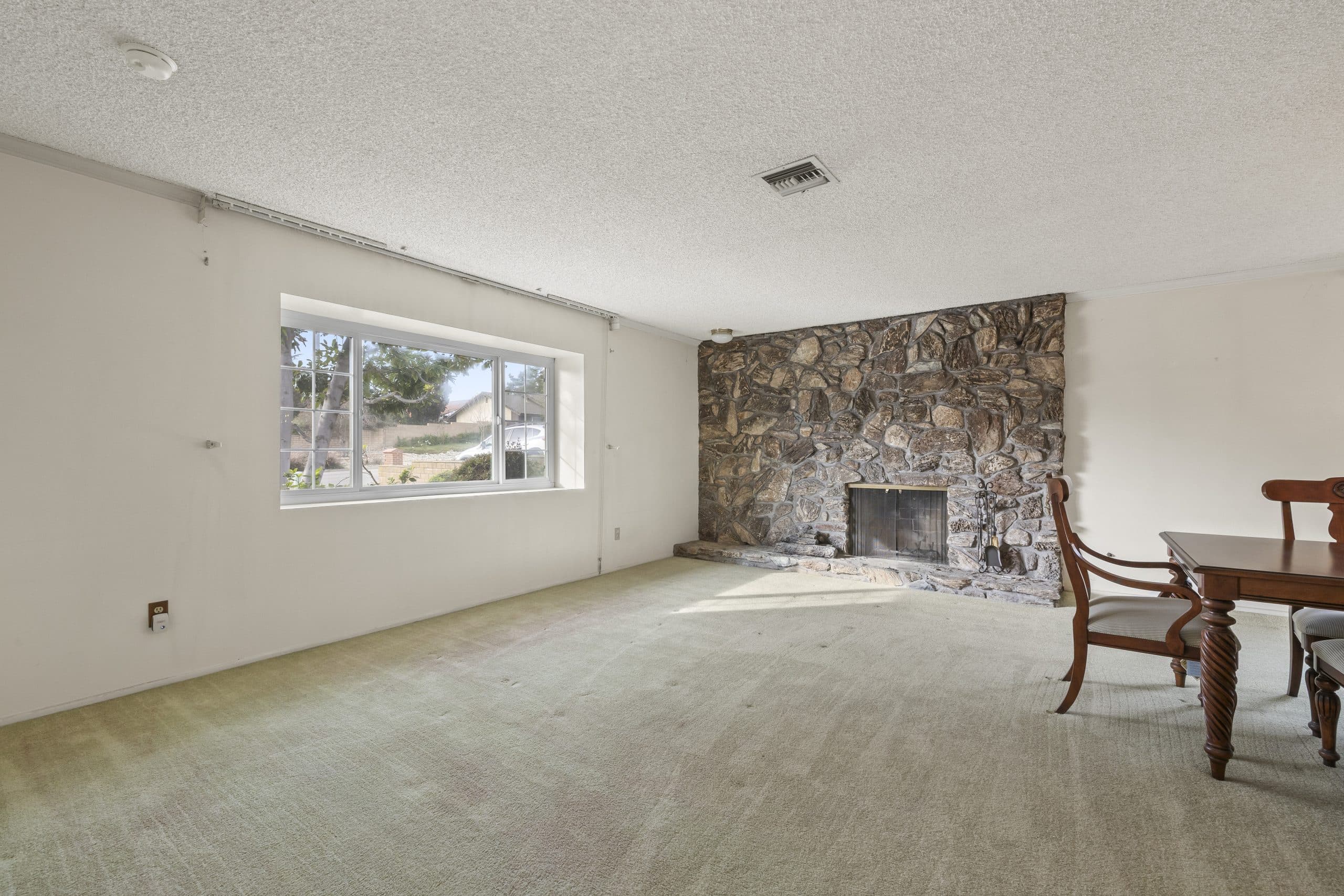 Vacant living room with a corner river-rock fireplace and bay window in a Claremont home