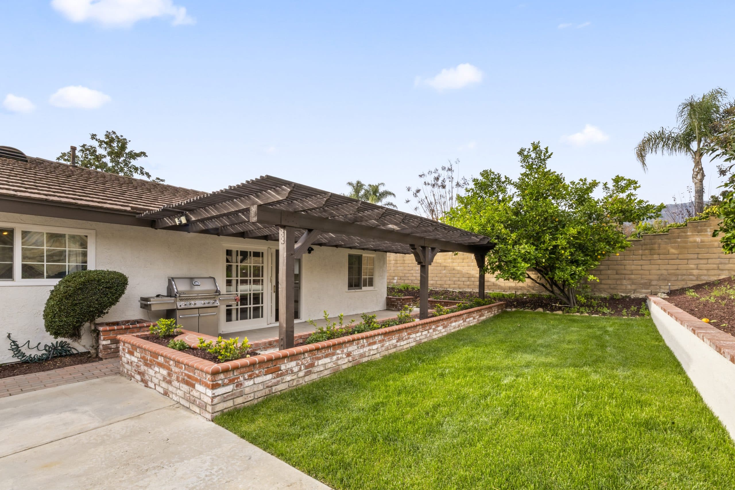 Manicured Claremont backyard with a pergola, brick planters, and citrus trees