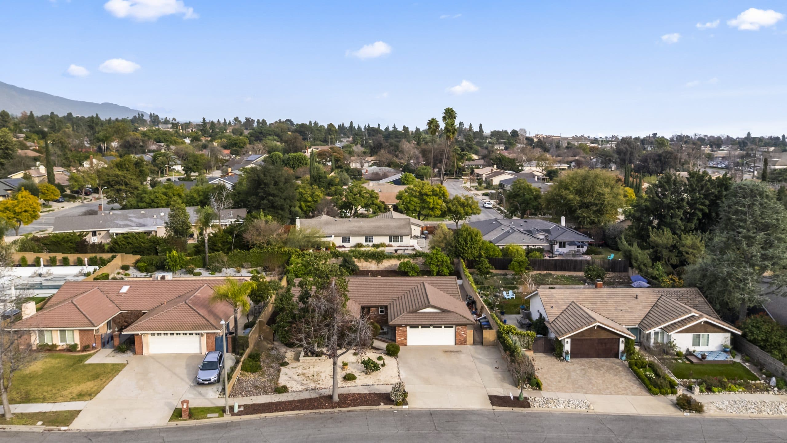Aerial view of a Claremont residential neighborhood with tile roofs, tree canopy, and mountains beyond