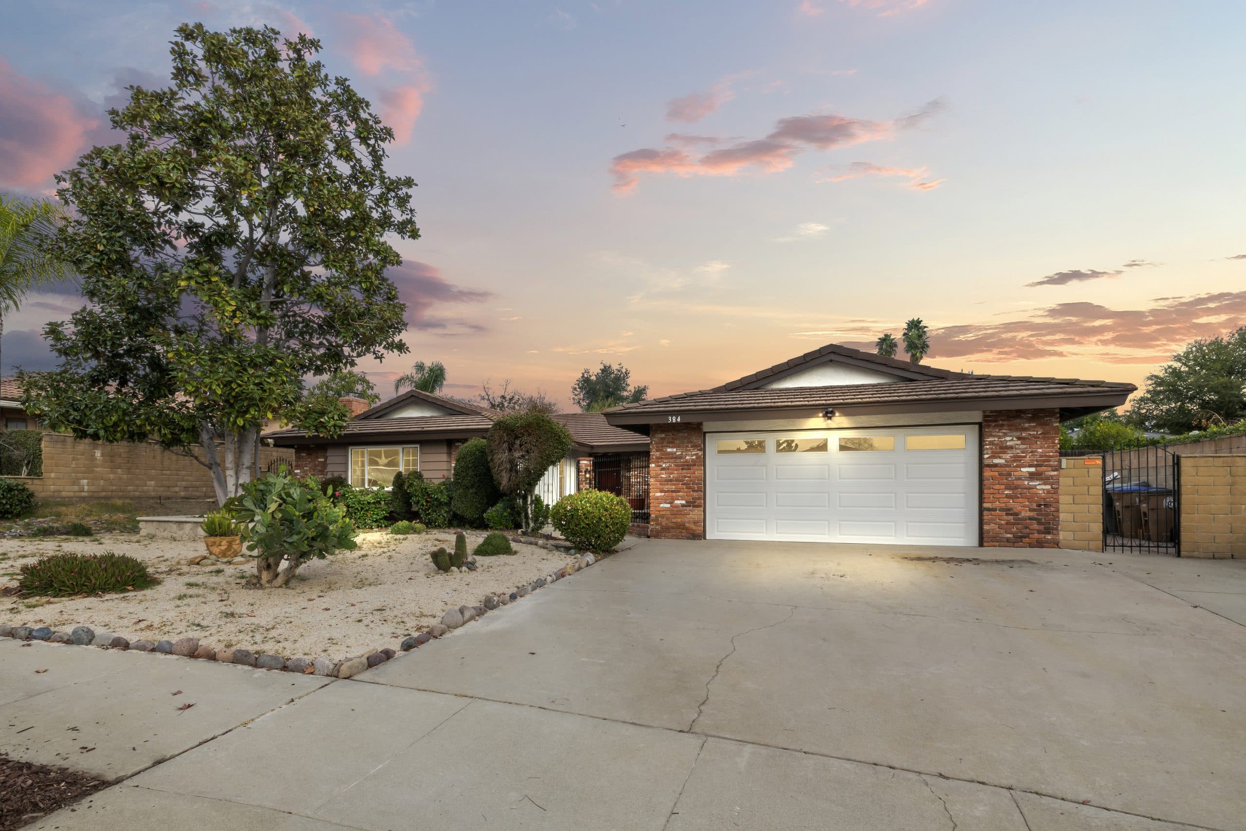 Claremont home at dusk with lit garage door windows, brick trim, and mature magnolia tree