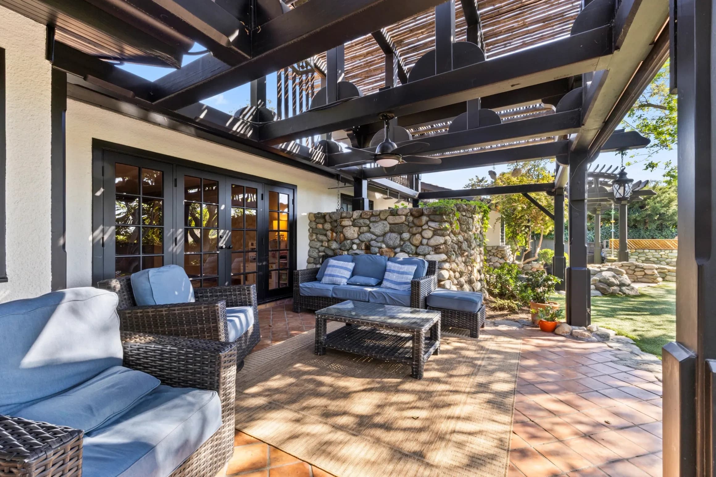 Covered patio with wicker seating and stone walls at a Claremont home