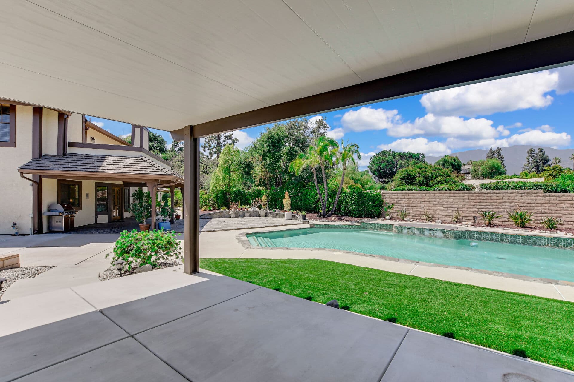 View from a shaded covered patio toward the pool and lawn of a Claremont home