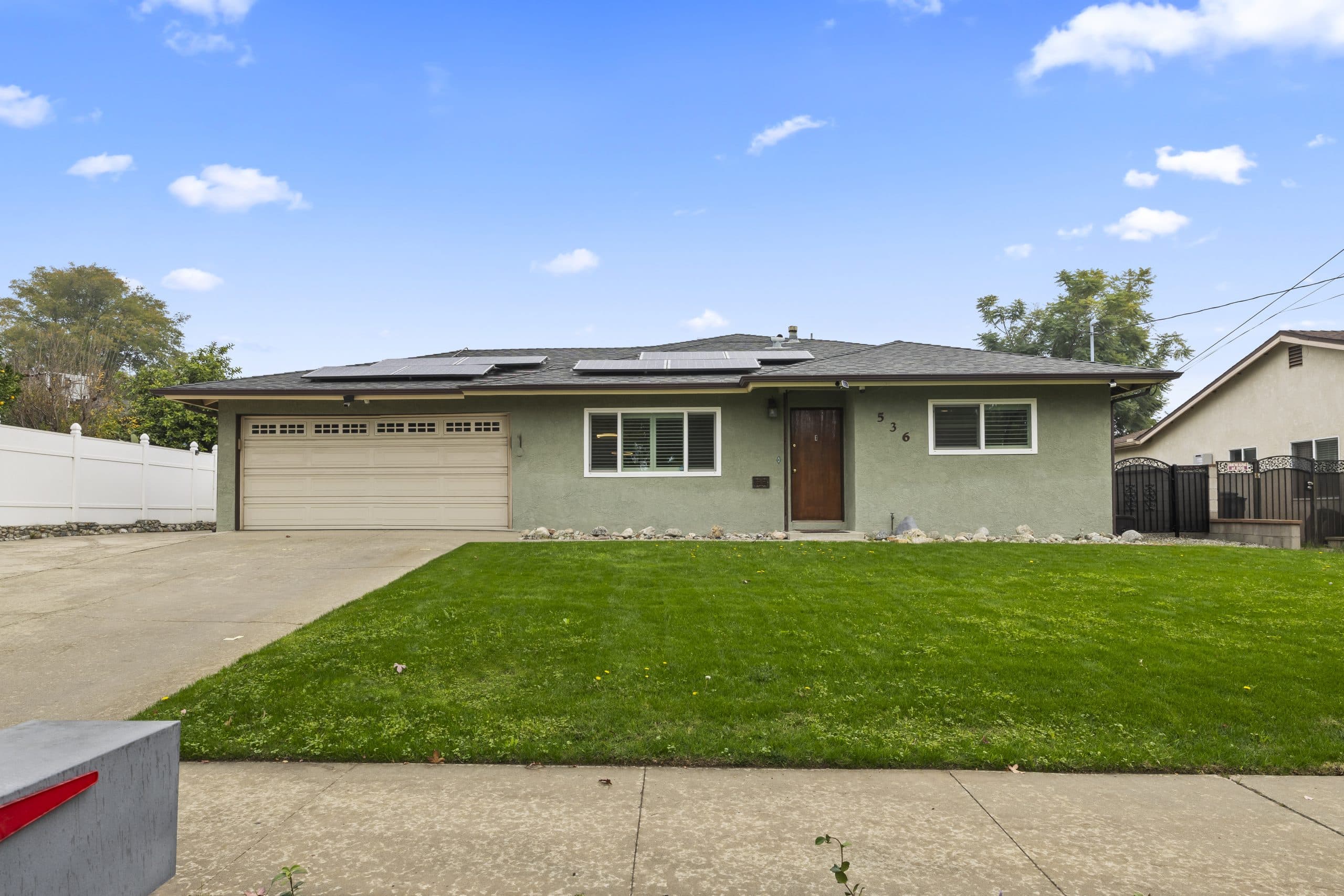 Green single-story Claremont ranch house with solar panels and a wide front lawn
