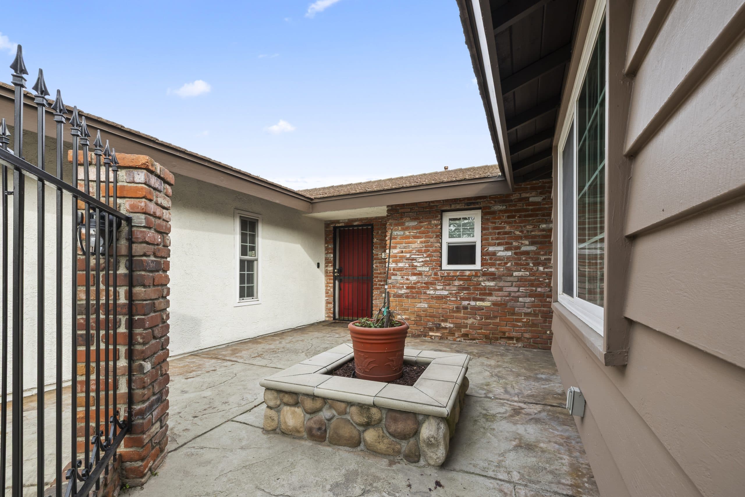 Front-entry courtyard of a Claremont home with a red door and brick planter wall