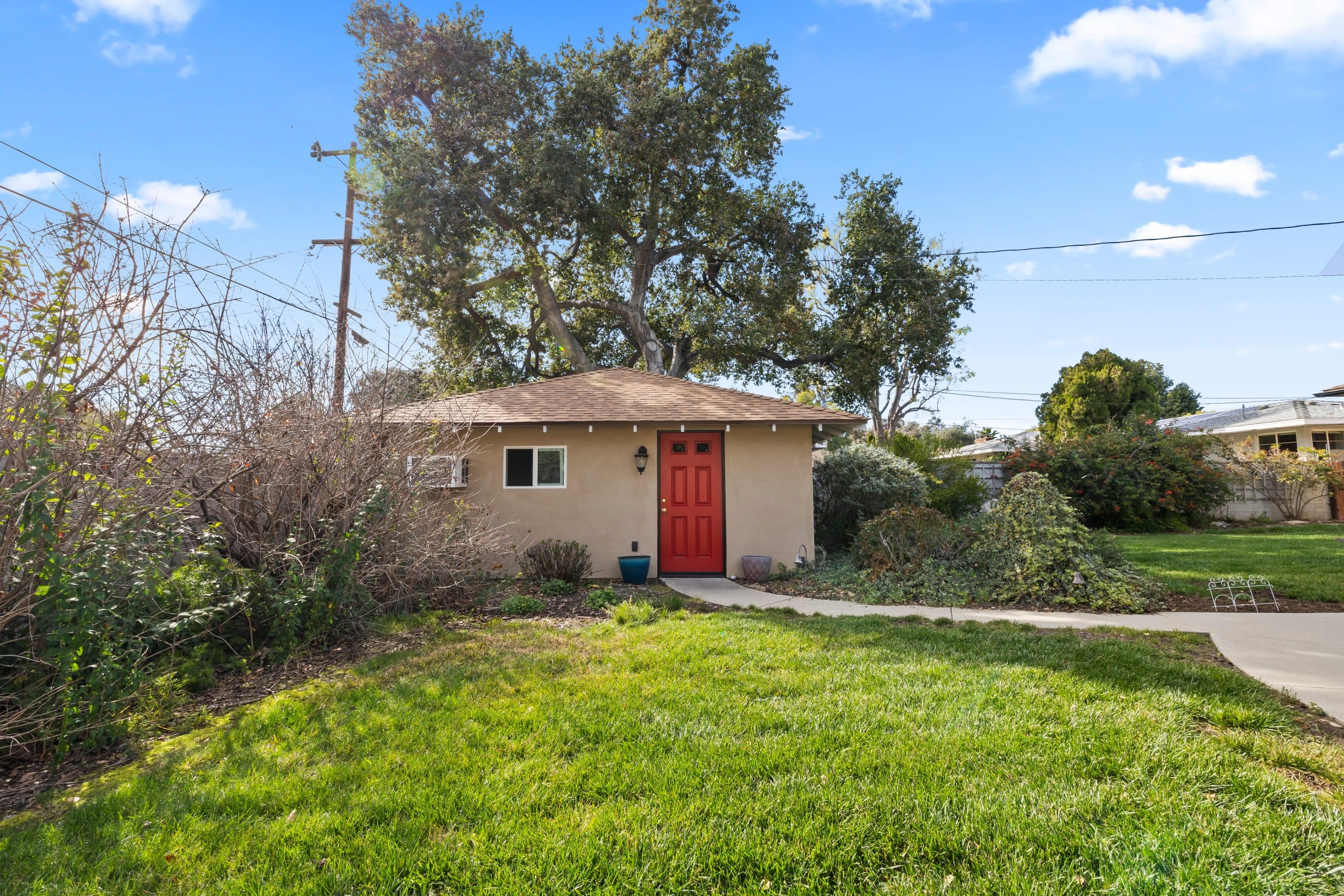 Small detached cottage with a red door on a Claremont lot, the scale of a typical backyard ADU